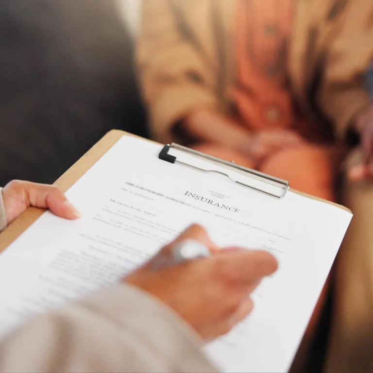 People talking with a piece of paper with the words insurance written on the paper attached to a clipboard.