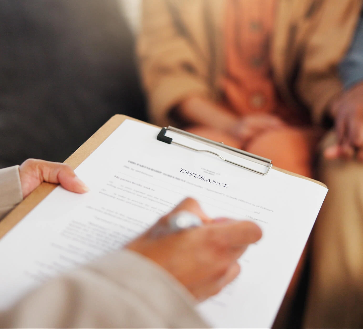 People talking with a piece of paper with the words insurance written on the paper attached to a clipboard.